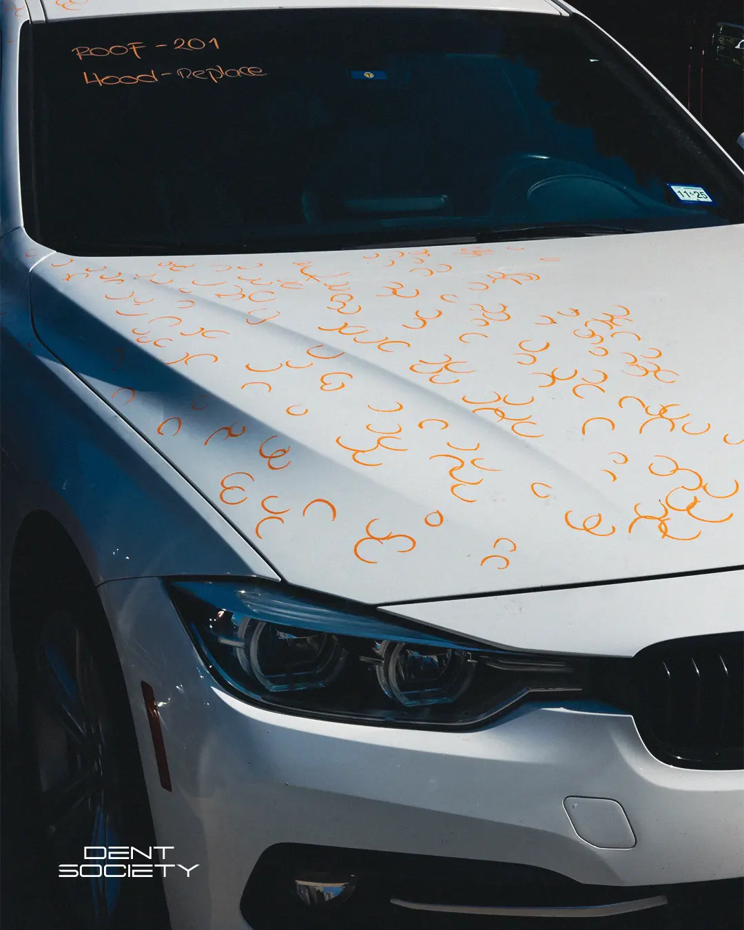 Hail damage marked for paintless dent repair inspection on white BMW
